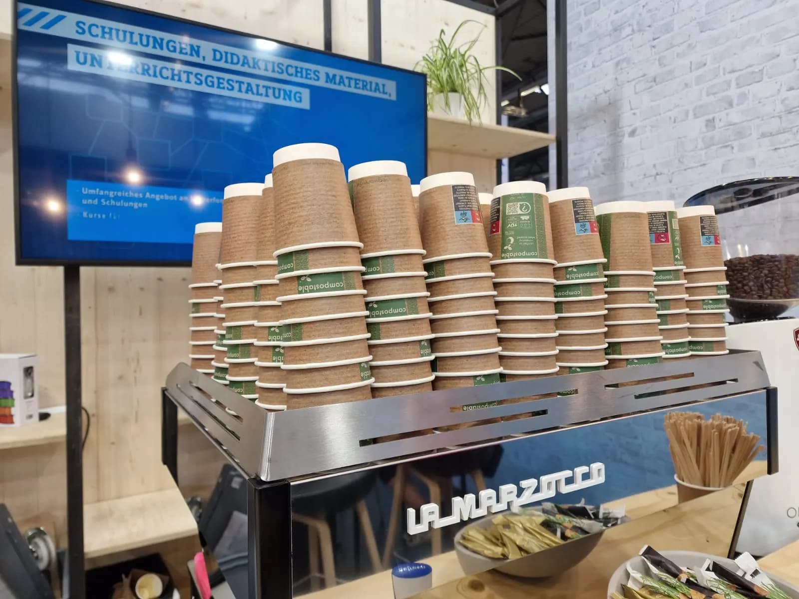 Siebträgermaschine auf einem Messestand, darauf gestapelte Kaffeebecher