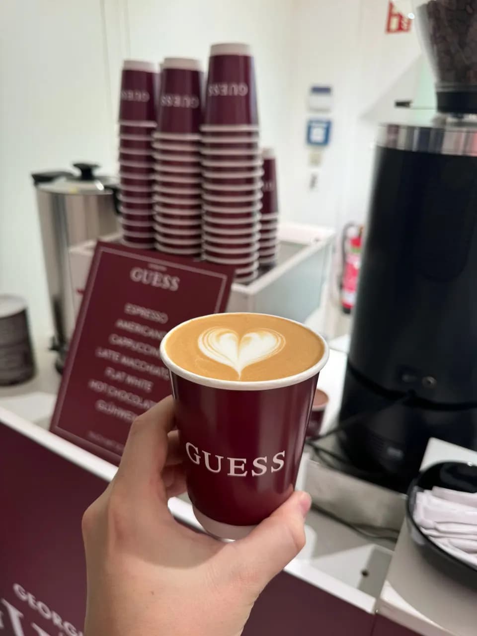 Gebrandeter To-go-Becher mit Latte-Art-Herz vor der Menütafel des Kunden