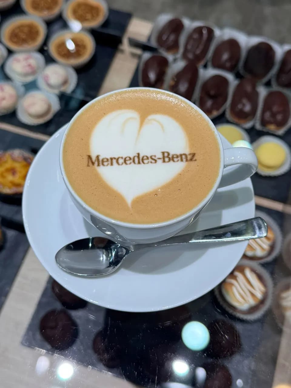 Cappuccino mit dem Schriftzug des Kunden im Milchschaum, daneben ein Dessertbuffet