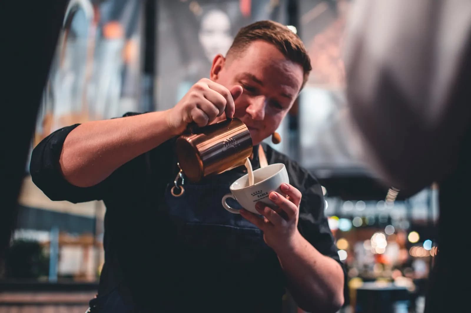 Barista gießt Milch aus einem Kännchen in eine Tasse