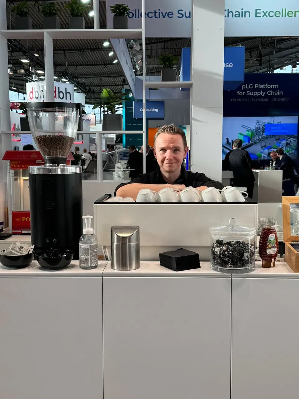 Barista hinter einem weißen Tresen mit Kaffeemühle und vorgewärmten Tassen