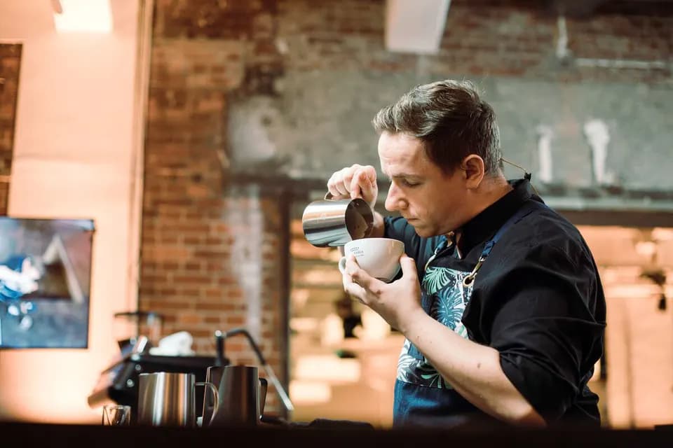 Kai Mößner gießt an der Bar Milchschaum in eine Tasse