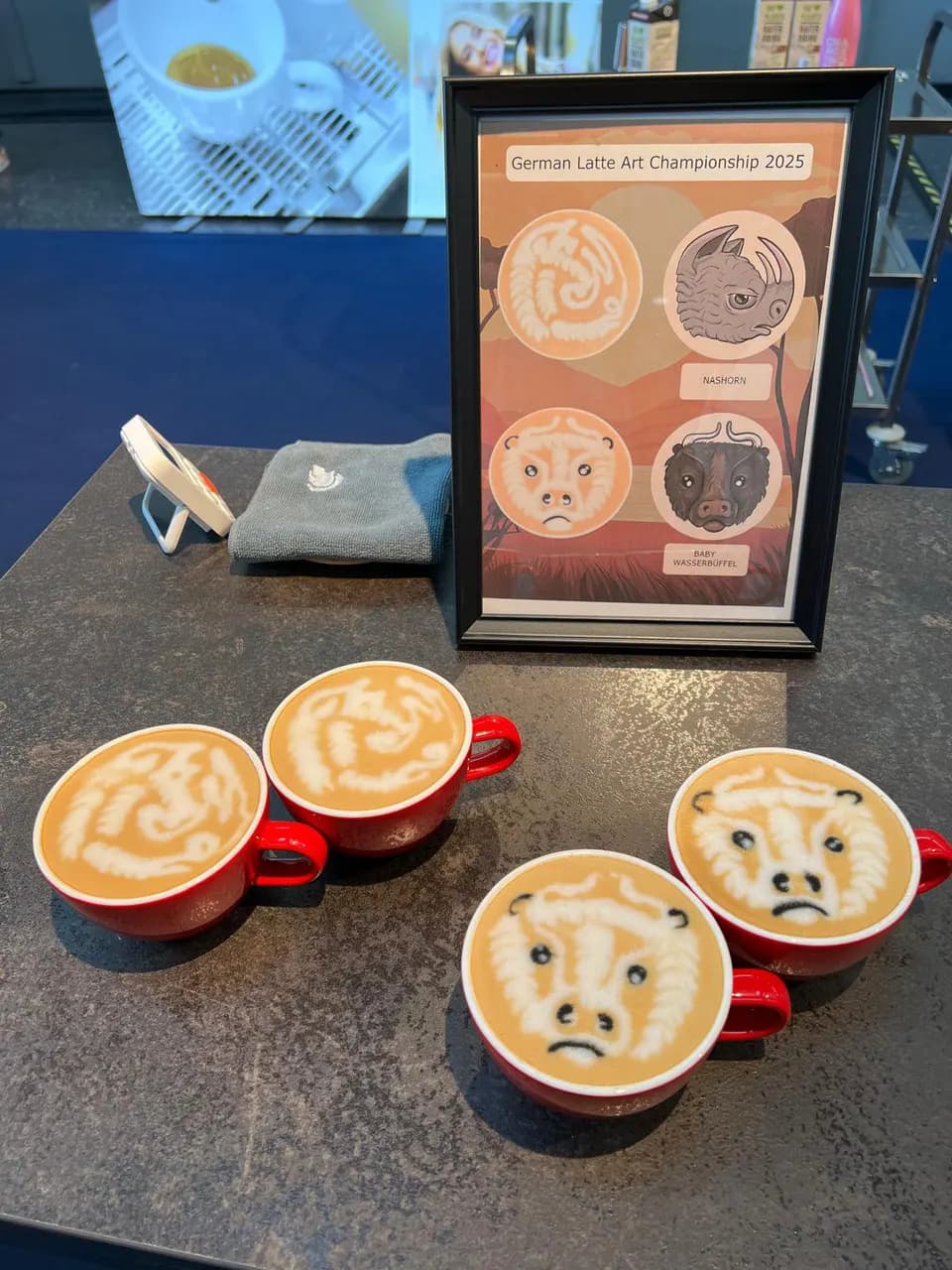 Latte-Art-Motive in Wettbewerbstassen vor einer Meisterschaftstafel