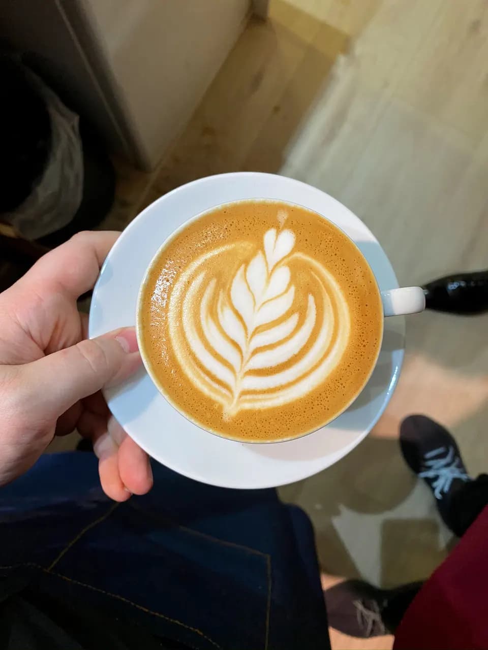 Cappuccino mit Latte-Art-Rosette in der Hand, von oben